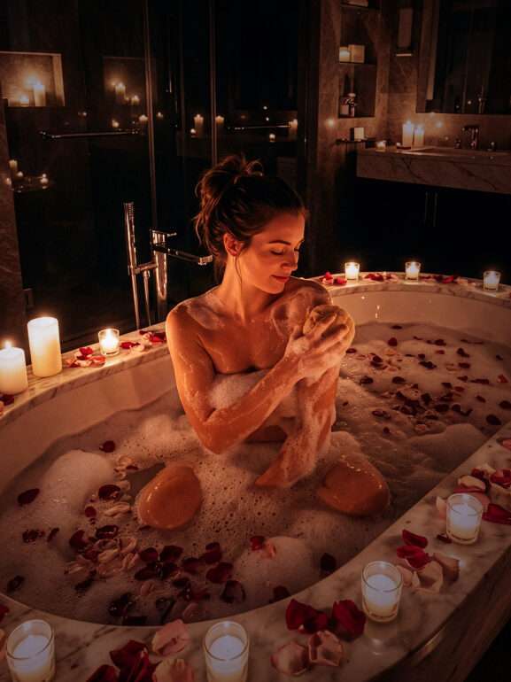 A woman that is bathing with soap and rose pedals.