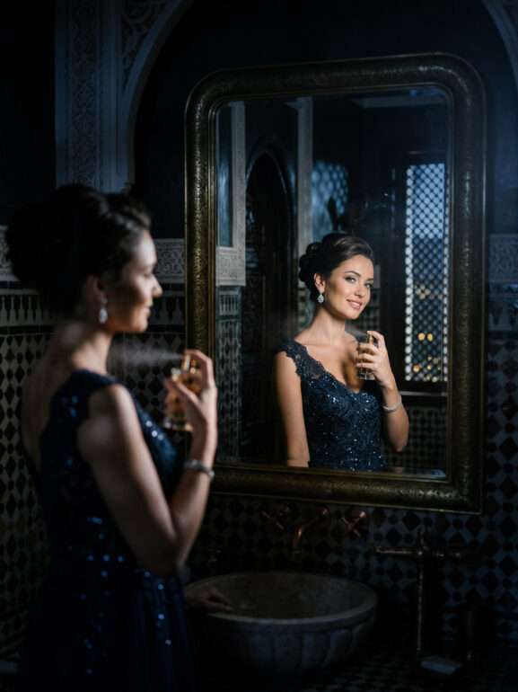 A beautiful woman looking in the mirror spraying her own perfume.
